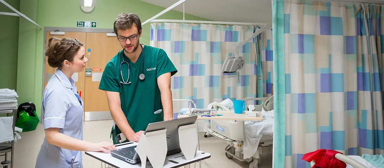 Hospital workers chat together whilst looking at a laptop