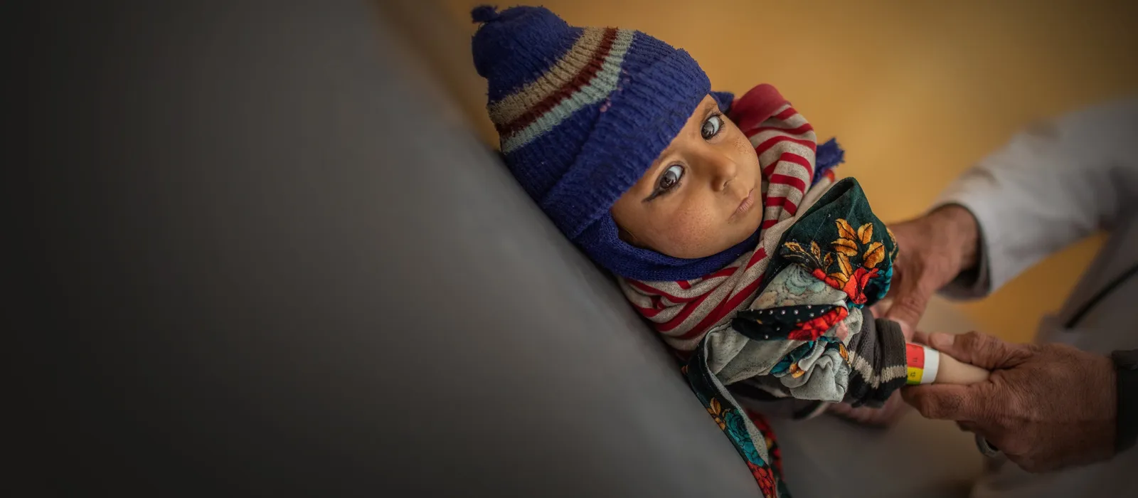 Baby with wooly hat led down with his hands being help