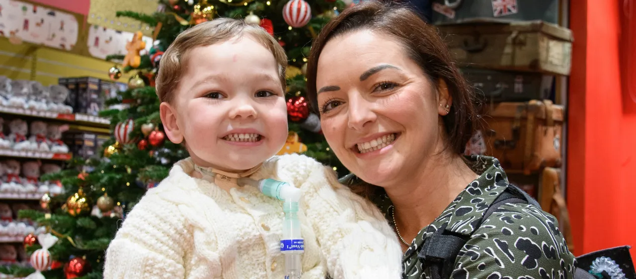 Lady holds little boy in front of Christmas tree at Great Ormond Street Hospital