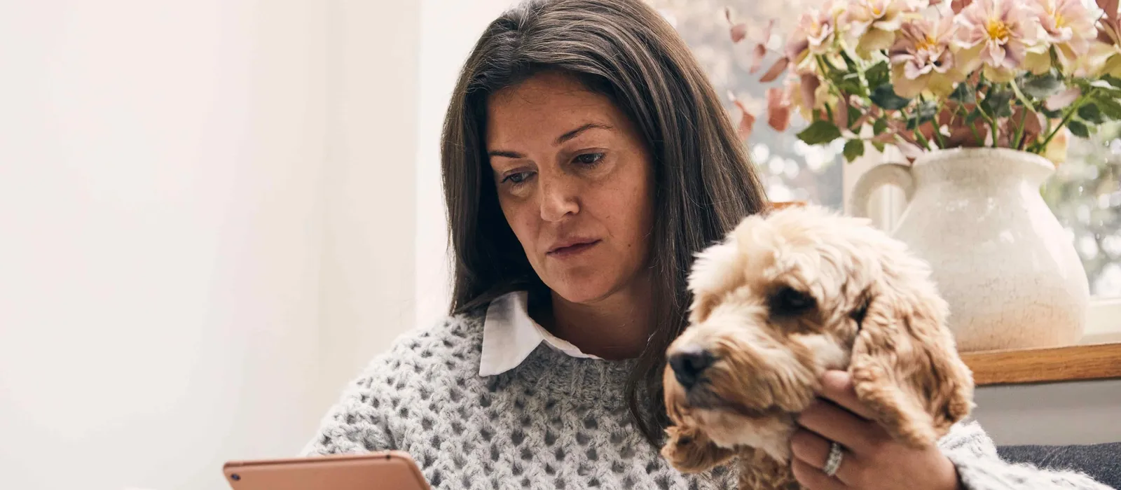 Sue Ryder's Image of a women looking at a tablet with a black dog on her lap.