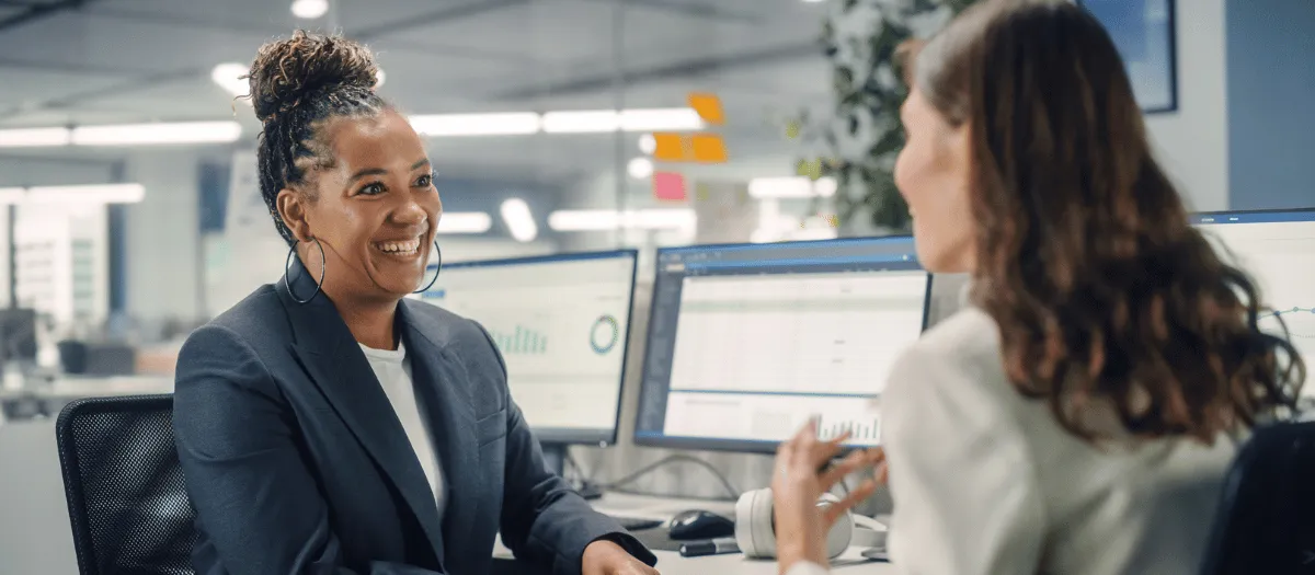 Two women chat in office in front of computer