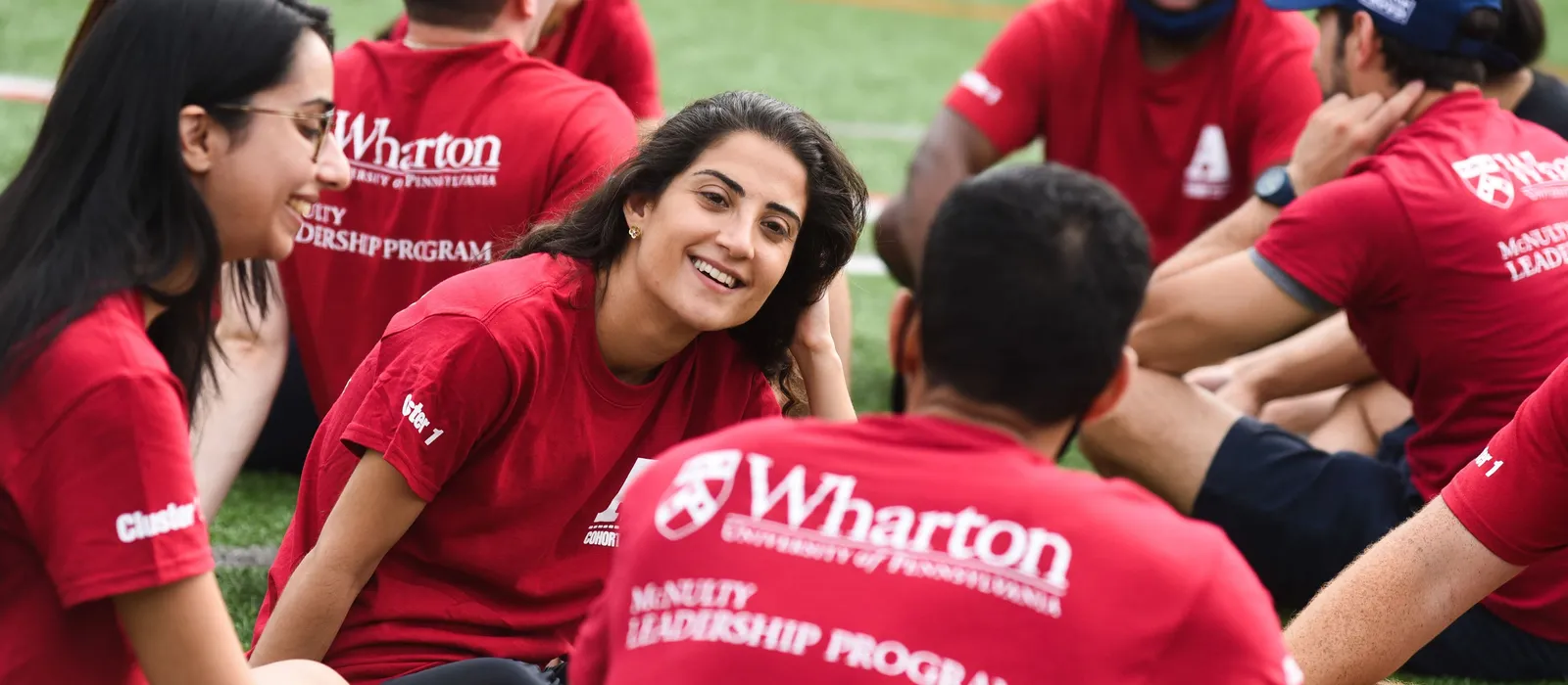 Young people sit together on field wearing red Wharton School University of Pennsylvania t-shirts