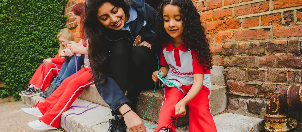 Lady helps little girl wearing 'Rainbows' uniform