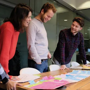 The team stand over the table to read coloured sticky notes